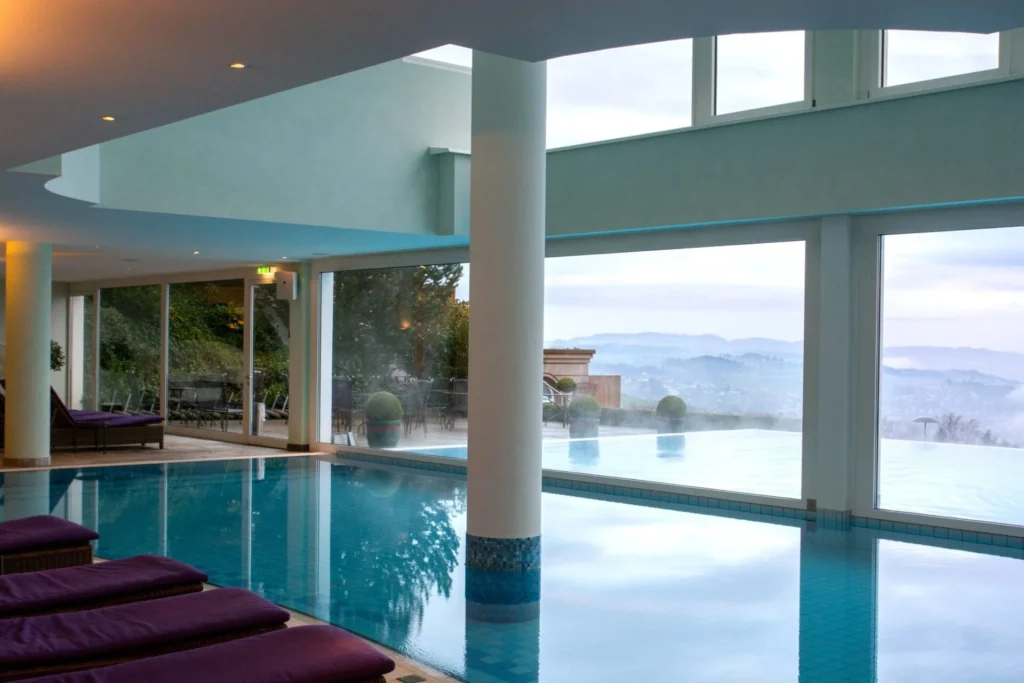 Innen-Infinity-Pool mit türkisem Mosaikband und Panoramablick über Feusisberg