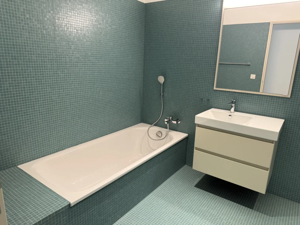 Grün gefliestes Badezimmer mit eingefliesster Badewanne und Waschtisch