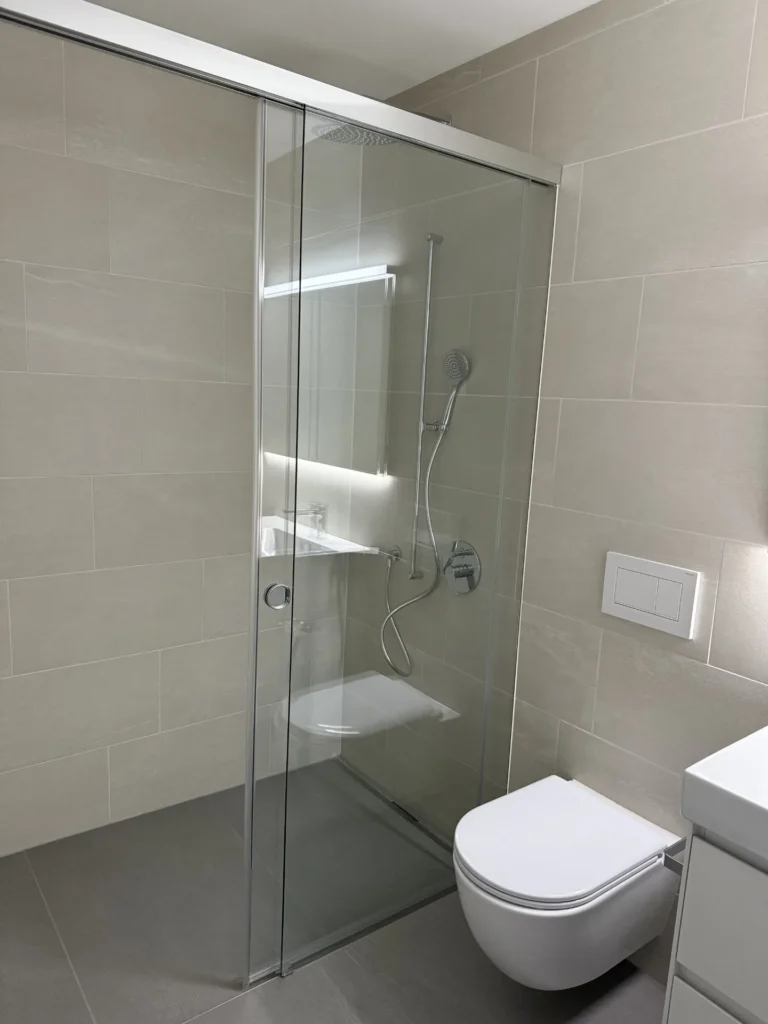 Bodengleiche Glasdusche mit Regendusche und beiger Steinoptikfliese