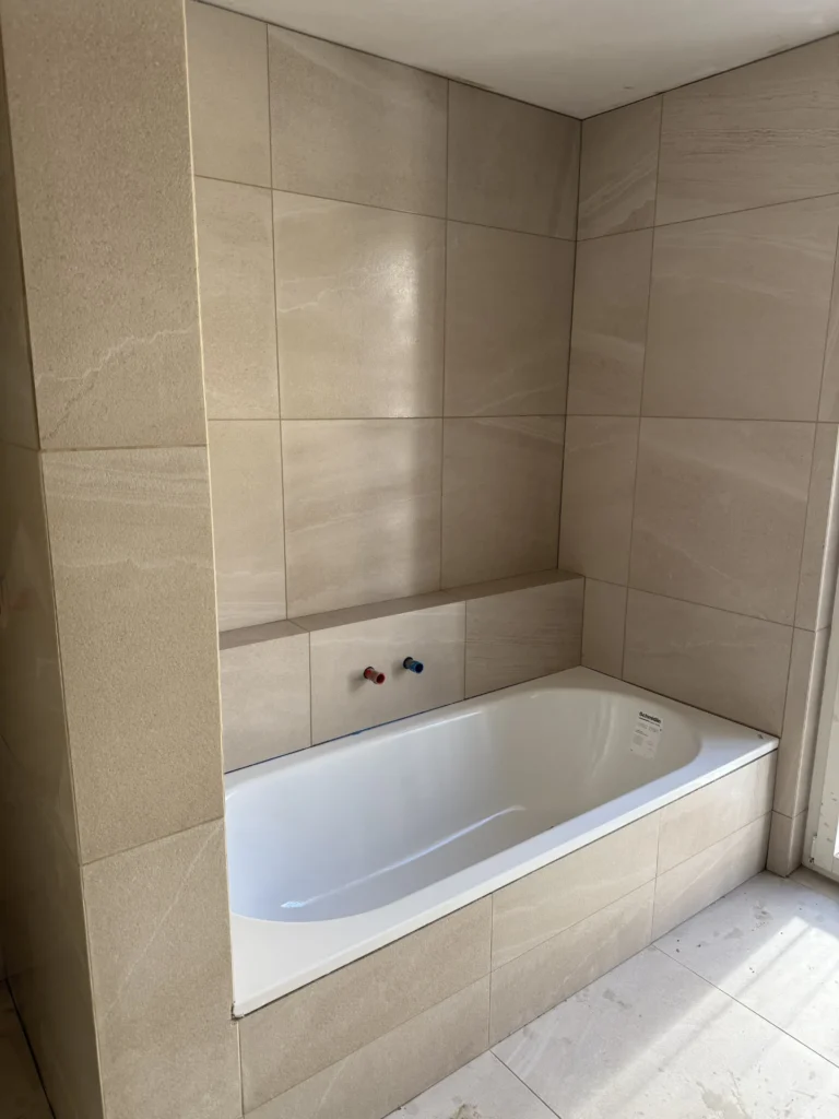 Eingefliesste Badewanne in beiger Naturstein-Optik mit Grossformatfliesen