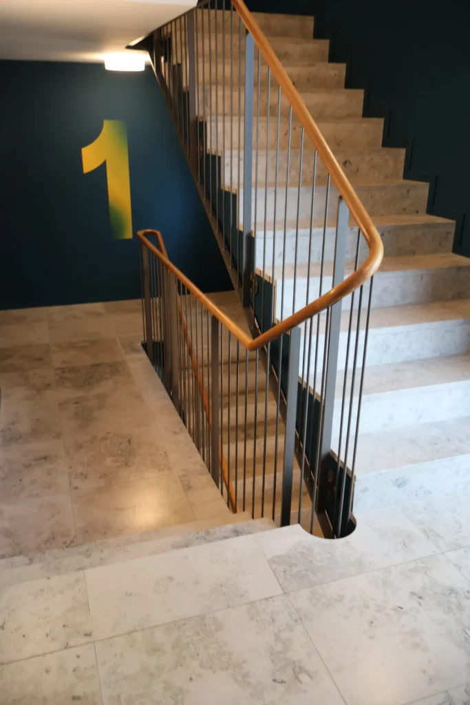 Natursteintreppe mit Holzhandlauf und Etagenkennzeichnung Nummer eins