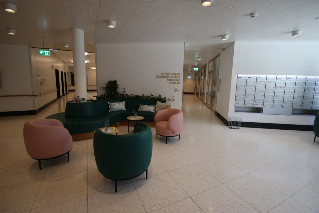 Loungebereich mit Kunststeinboden, farbigen Sesseln und Briefkastenanlage