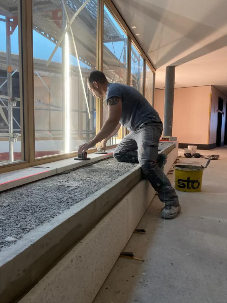 Plattenleger verlegt Kunststeinplatte auf Fensterbank im Rohbau