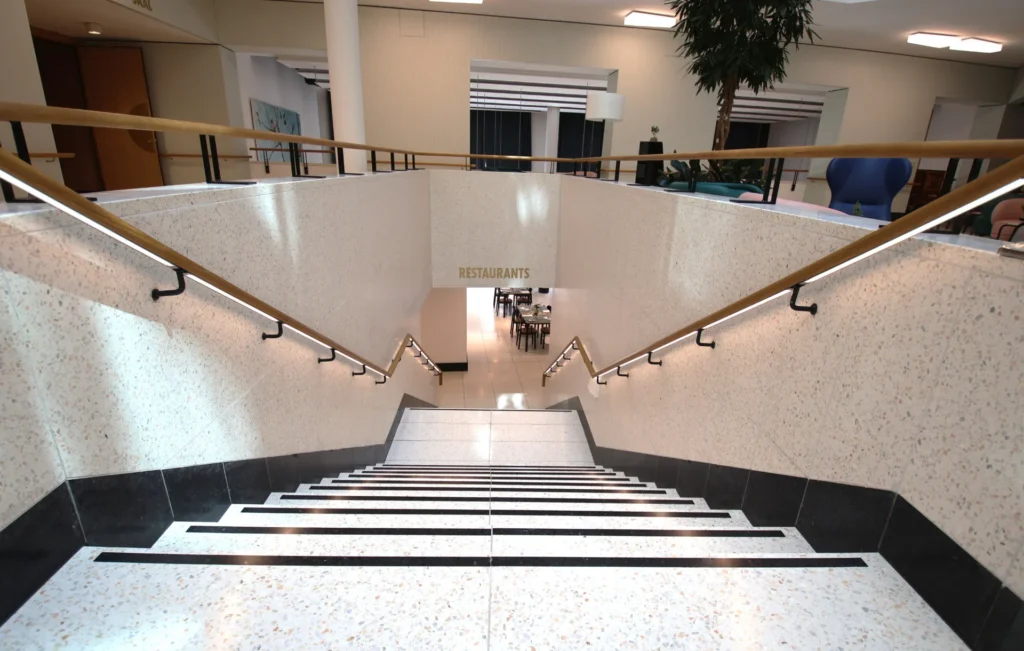 Breite Treppe mit Terrazzostufen und schwarzen Zierstreifen im Foyer