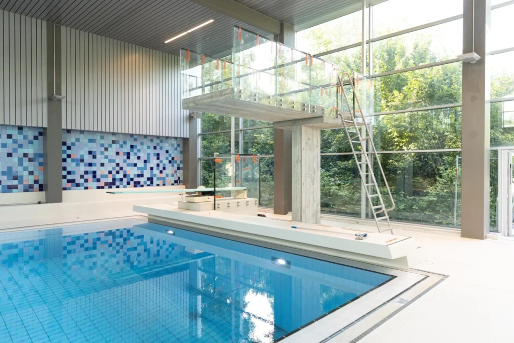Sprungbecken mit blauem Mosaik, Sprungturm und grosser Glasfassade