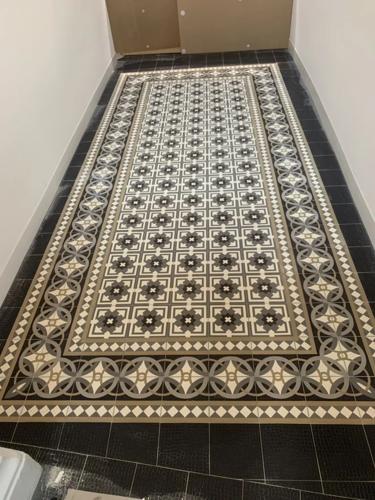 Ornamentaler Zementmosaik-Bodenteppich mit dunklen Blütenmustern und Zierbordüren