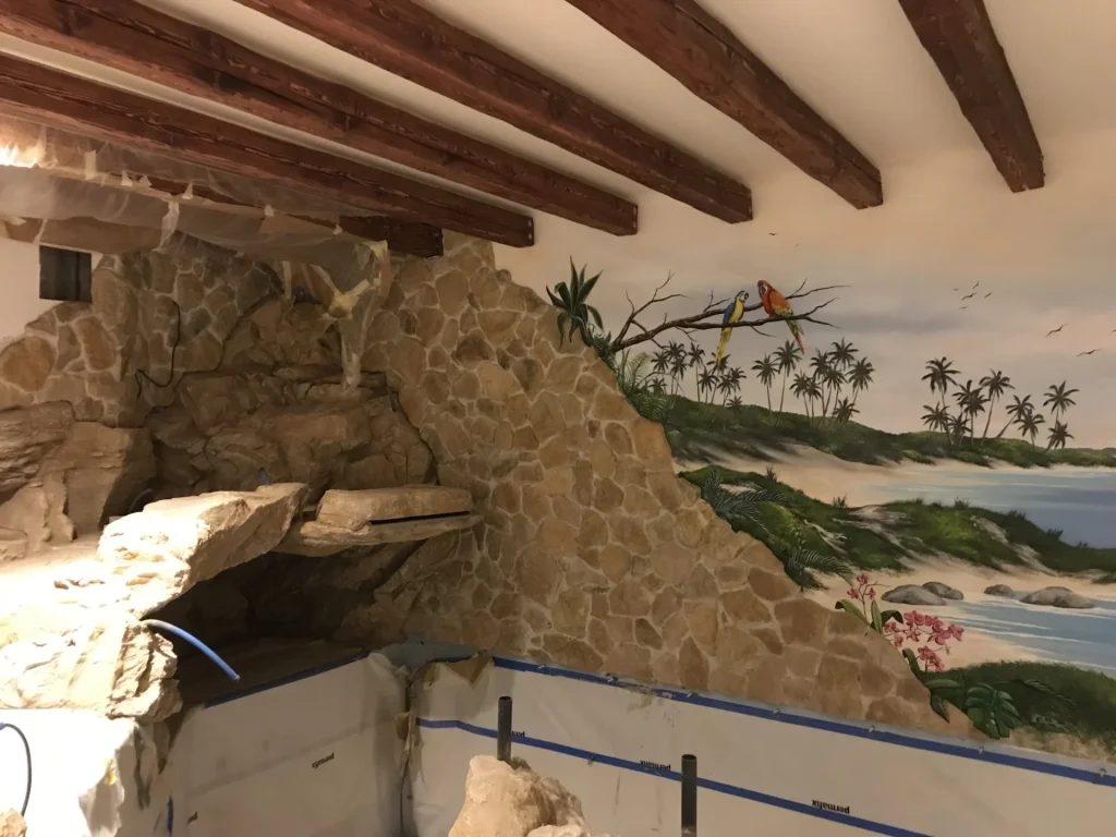 Natursteingrotte mit Wasserlauf und tropischer Wandmalerei