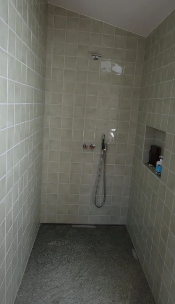 Dusche mit cremefarbenen quadratischen Keramikplatten und Natursteinboden
