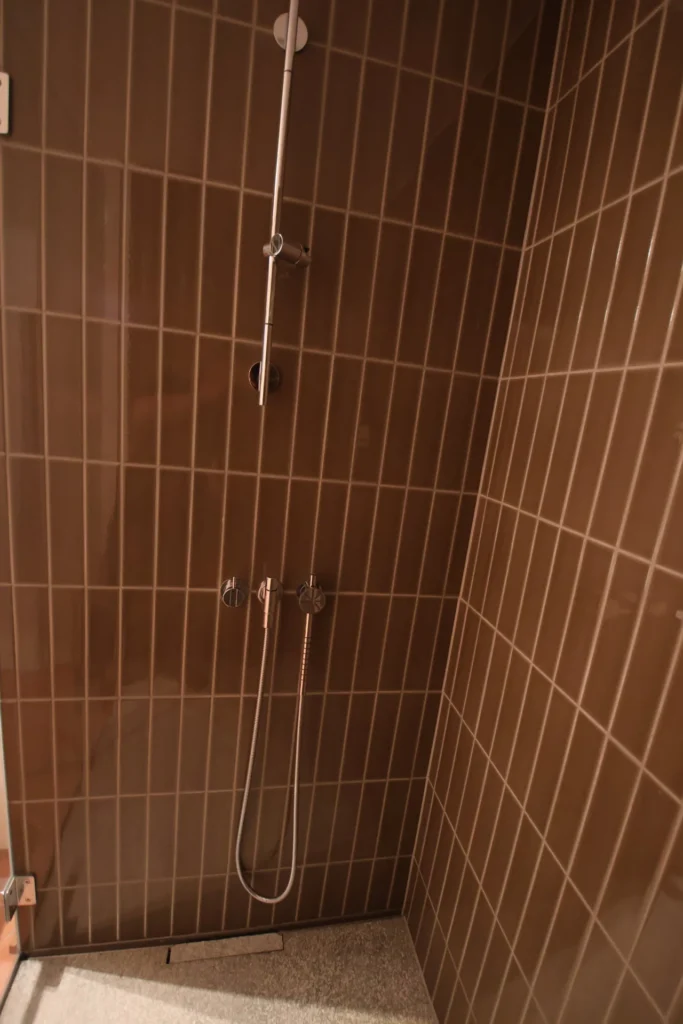 Dusche mit dunkelbraunen vertikalen Keramik-Riemchen und Handbrause