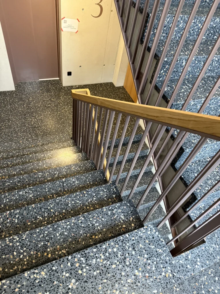 Terrazzo-Treppe anthrazit mit Holzhandlauf, Blick ins Treppenhaus